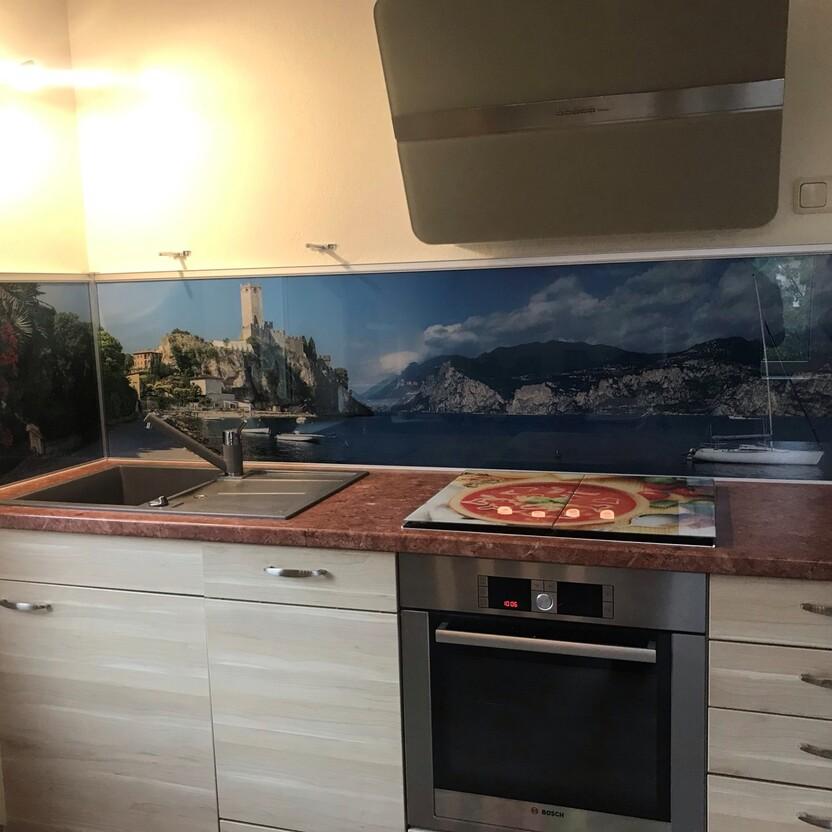 Küche nach Maß mit Landschafts-Motiv auf Glas, Edelstahlherd und Spüle mit Abtropffläche.