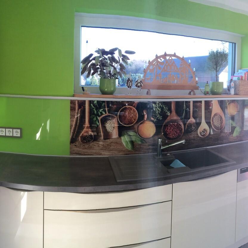 Küche nach Maß mit Gewürzmotiv auf Glasrückwand, grüner Wandfarbe und viel Stauraum.