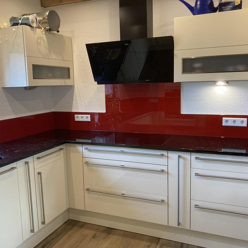 Küche nach Maß mit roter Glasnische, schwarzer Arbeitsplatte und modernen Griffleisten.