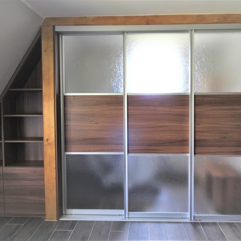Maßgefertigter Schiebetürenschrank unter Dachschräge, Kombination aus Glas und dunklem Holzdekor mit offenen Regalfächern.
