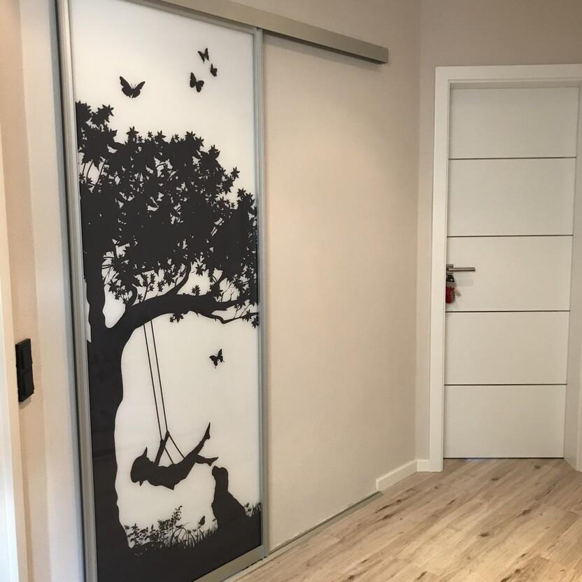 Schiebetür mit Glasdruck in Schwarz-Weiß, Motiv eines Mädchens auf einer Schaukel unter einem Baum mit Schmetterlingen, in modernem Flur.