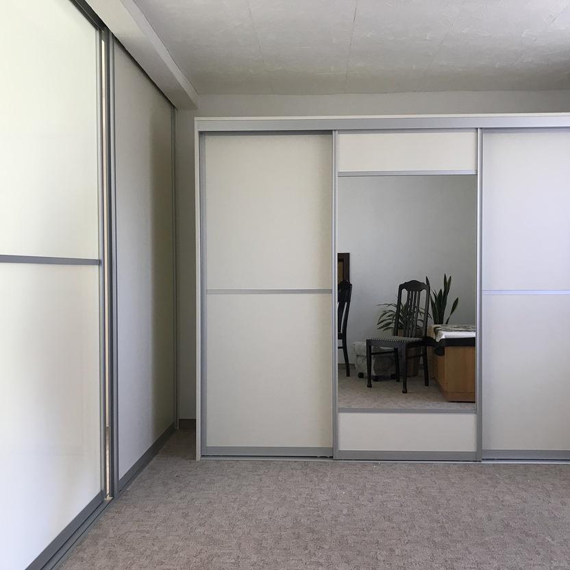 Großer weißer Schiebetürenschrank mit integriertem Spiegel in einem hellen Schlafzimmer mit grauem Teppichboden.