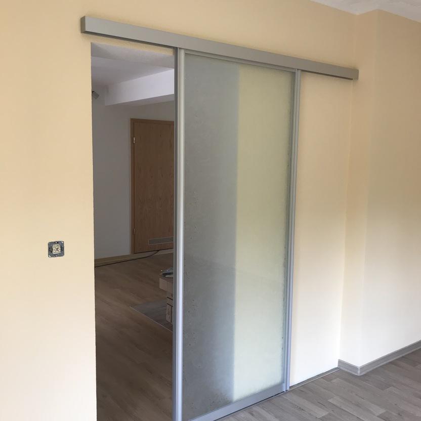 Schlichte, halbtransparente Schiebetür aus Milchglas mit Aluminiumrahmen in einem Raum mit hellgelben Wänden und Parkettboden.