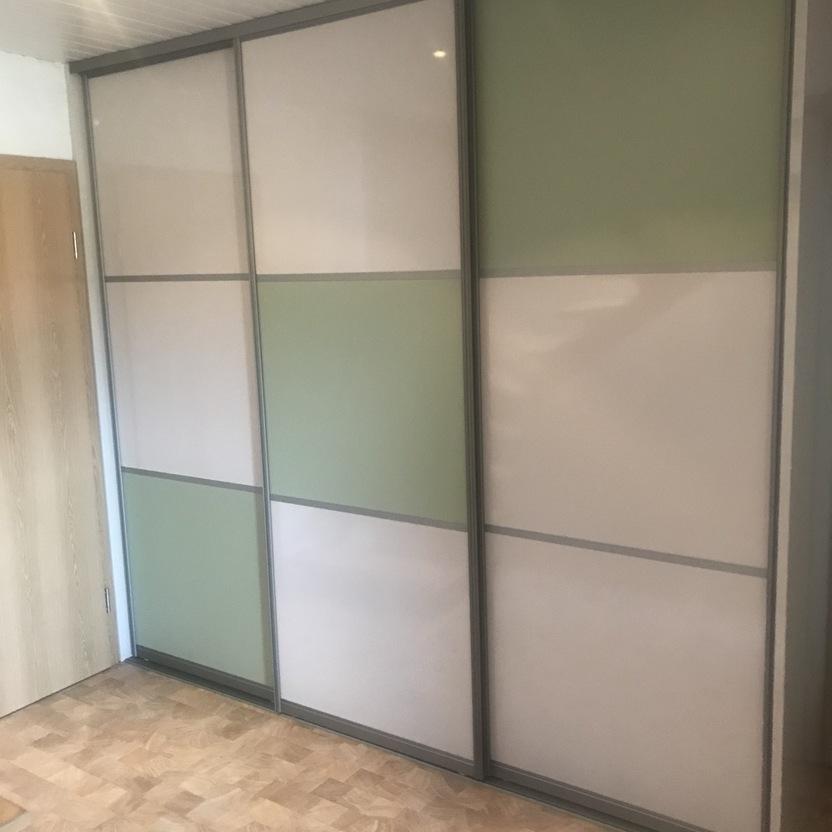 Moderner Schiebetürenschrank mit cremefarbenen und grünen Glasflächen in einem Raum mit hellem Holzfußboden und Holzdecke.