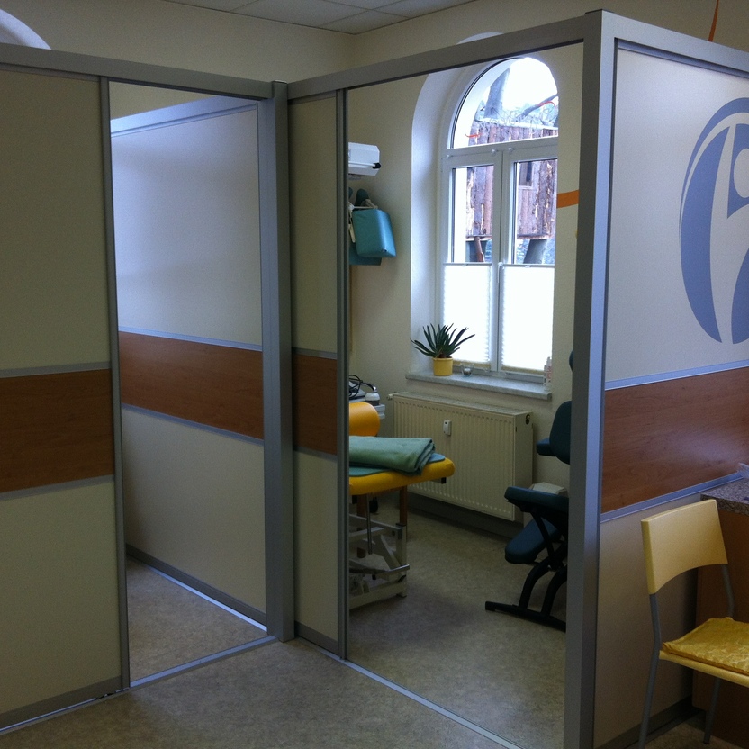 Raumtrennsystem mit Schiebetüren in Holz- und Glasoptik in einer Praxis, teilt Behandlungsbereiche mit integriertem Logo.