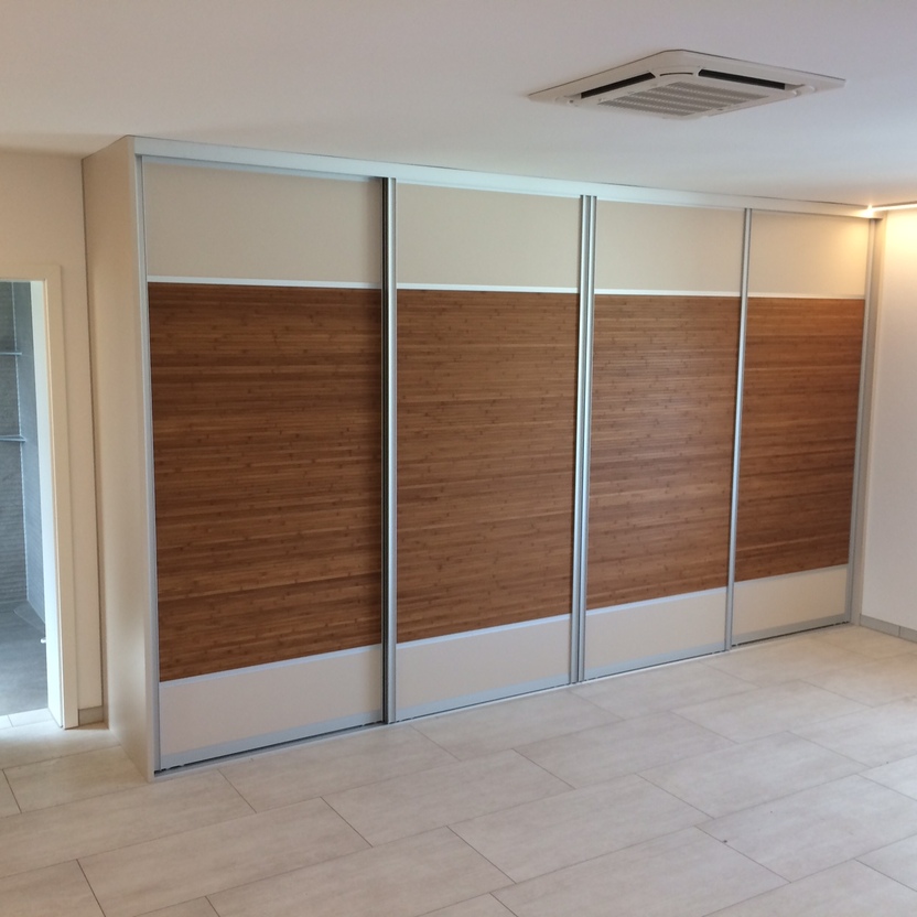 Moderner Einbauschrank mit Schiebetüren in Holzoptik und hellen Paneelen in einem Raum mit Fliesenboden und Zugang zum Bad.