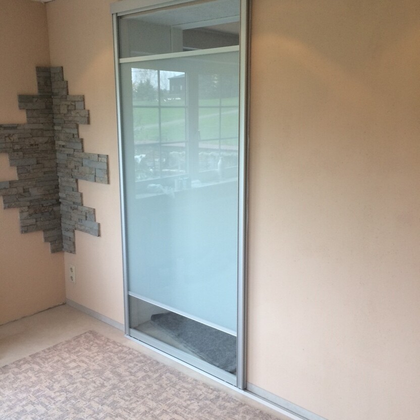 Halbtransparente Schiebetür mit Aluminiumrahmen in hellbeigem Raum, kombiniert mit Natursteinwand und Teppichboden.