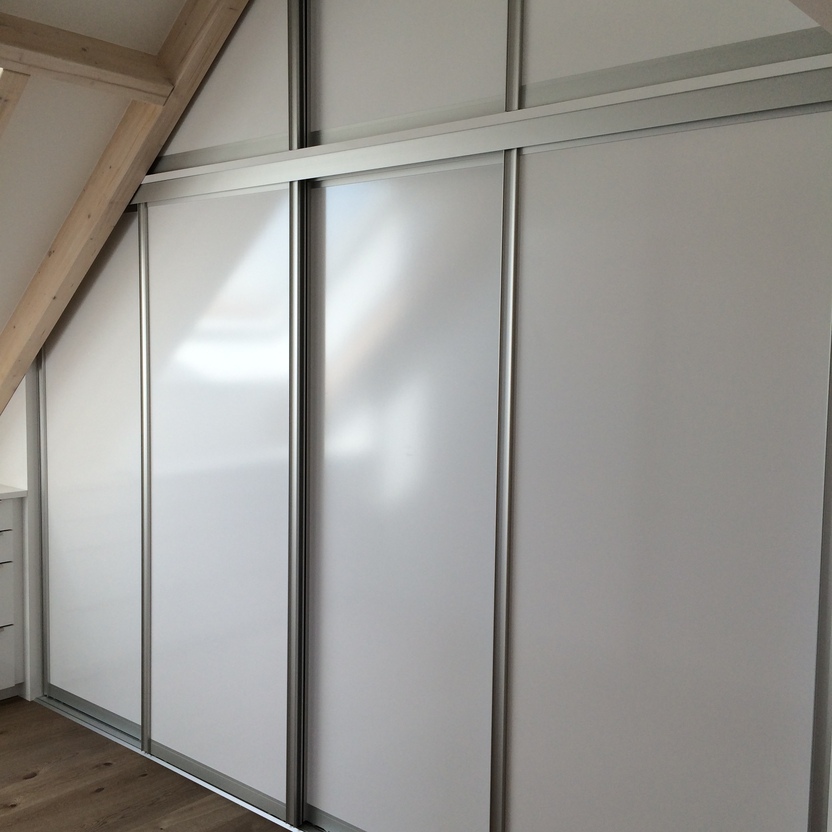 Großer weißer Einbauschrank mit Schiebetüren und Aluminiumrahmen, passgenau unter Dachbalken montiert.