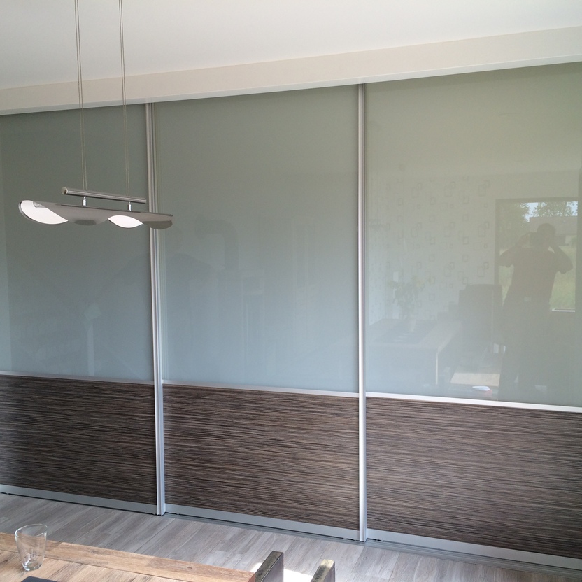 Großflächiges Schiebetürsystem mit Milchglas und dunklem Holzdekor, trennt Essbereich und Wohnzimmer in moderner Einrichtung.