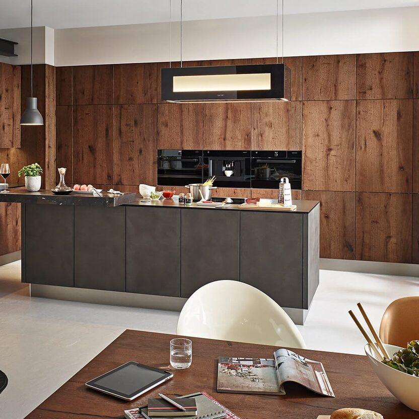 Küche nach Maß mit Kochinsel, dunklen Fronten, Holzwand und eleganter Beleuchtung.