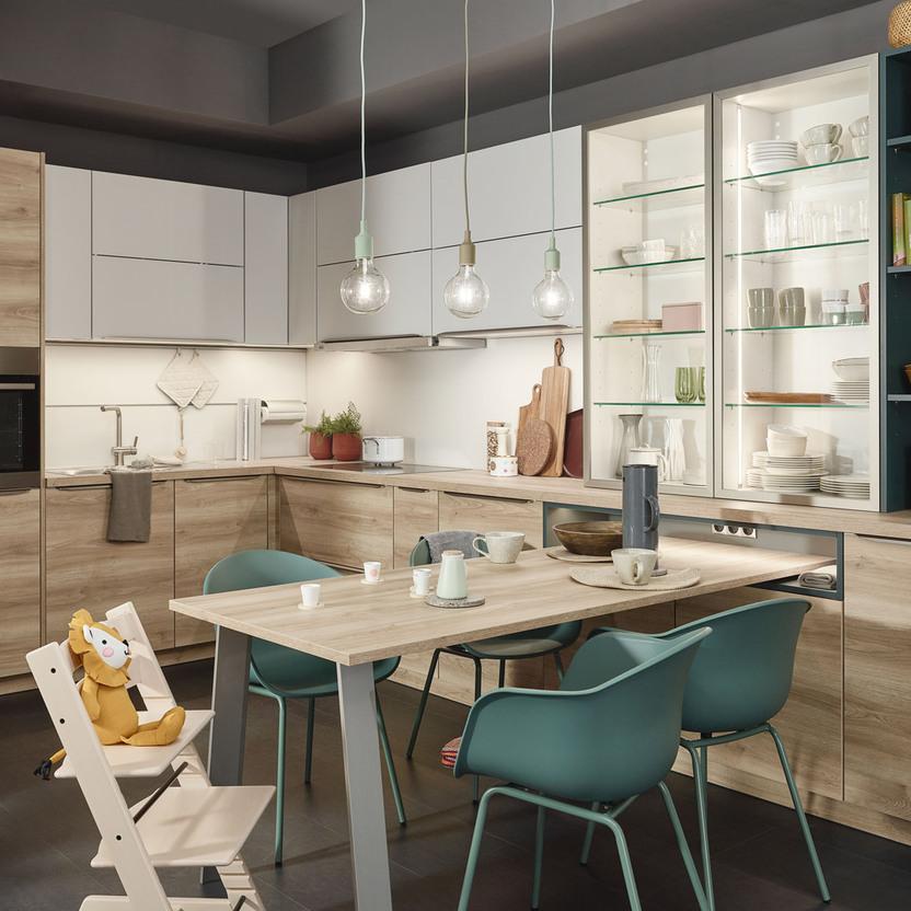 Küche nach Maß in Holzoptik mit Glashängeschränken, Bücherregal und großem Esstisch.
