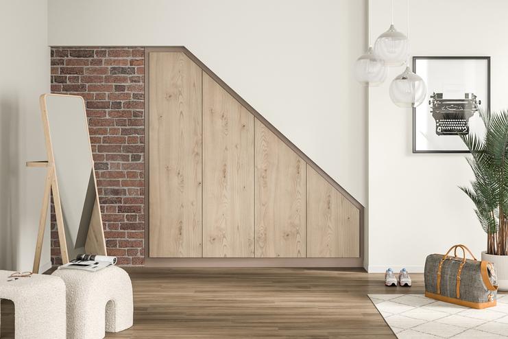 Ein großer, eingebauter Wandschrank nach Maß mit hellen Holzfronten, integriert in eine Dachschräge neben einer Ziegelwand.